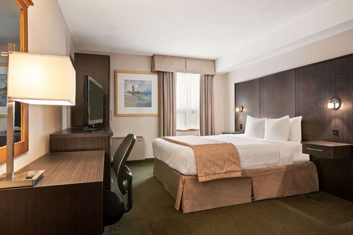 A hotel room with a bed, desk, chair, television, and artwork on the wall.