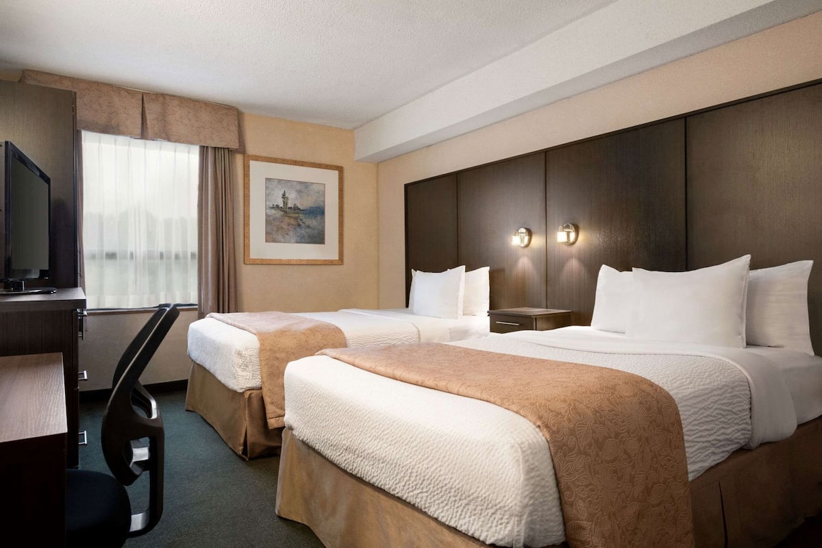 A hotel room with two beds, a desk, a television, and a painting on the wall.
