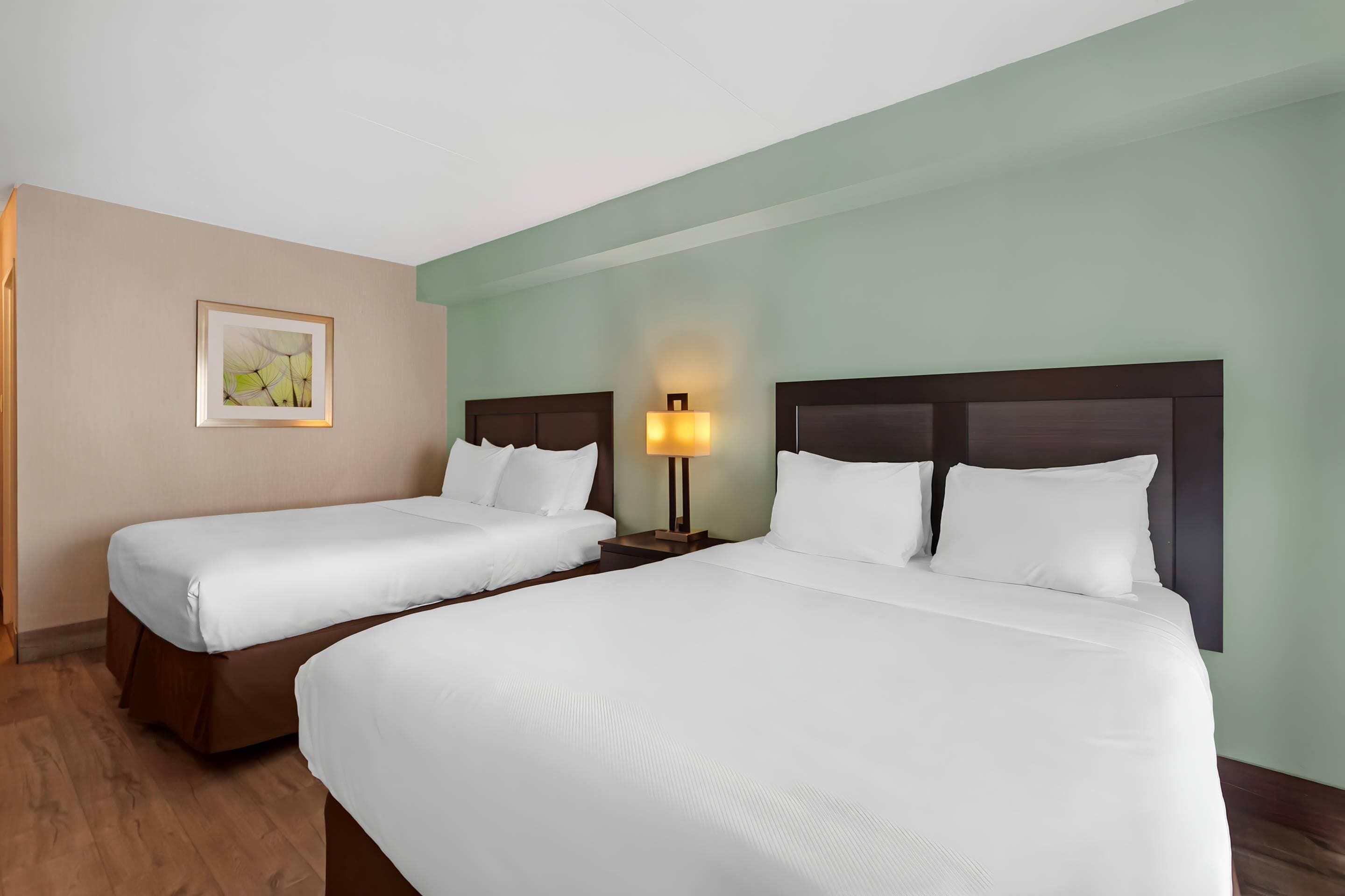 A hotel room with two beds, a nightstand with a lamp, and a framed picture on the wall.
