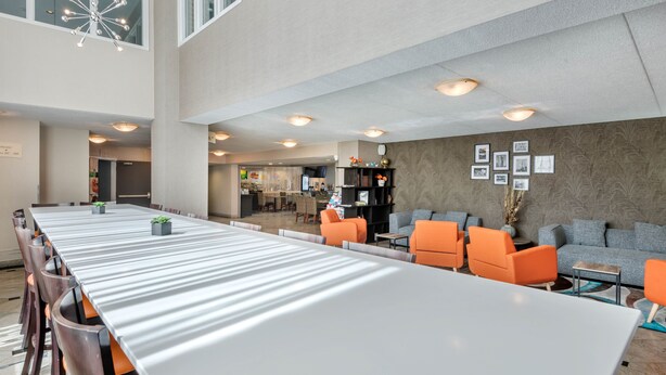A spacious conference room with a long table and modern chairs, a seating area with orange sofas, and a decorative wall with framed pictures.