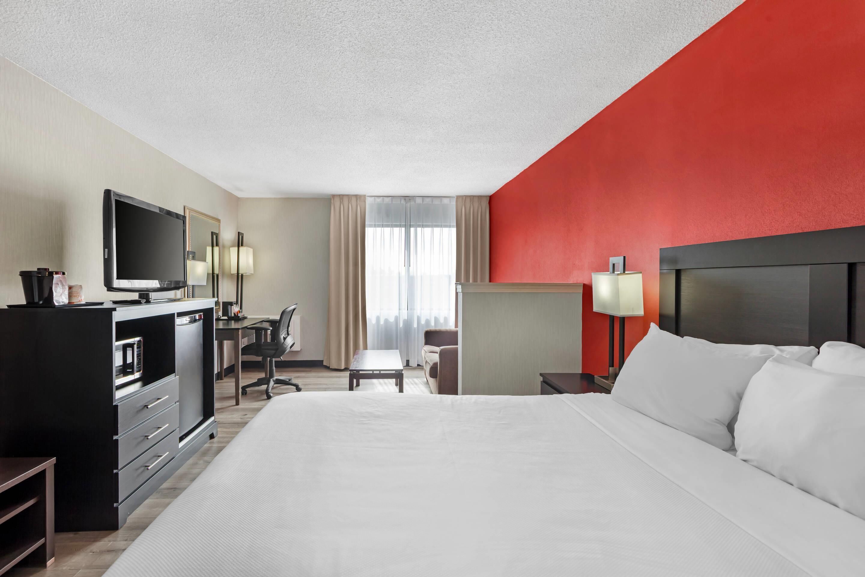 Une chambre d’hôtel avec un grand lit, un bureau avec un ordinateur, une télévision et un minibar.