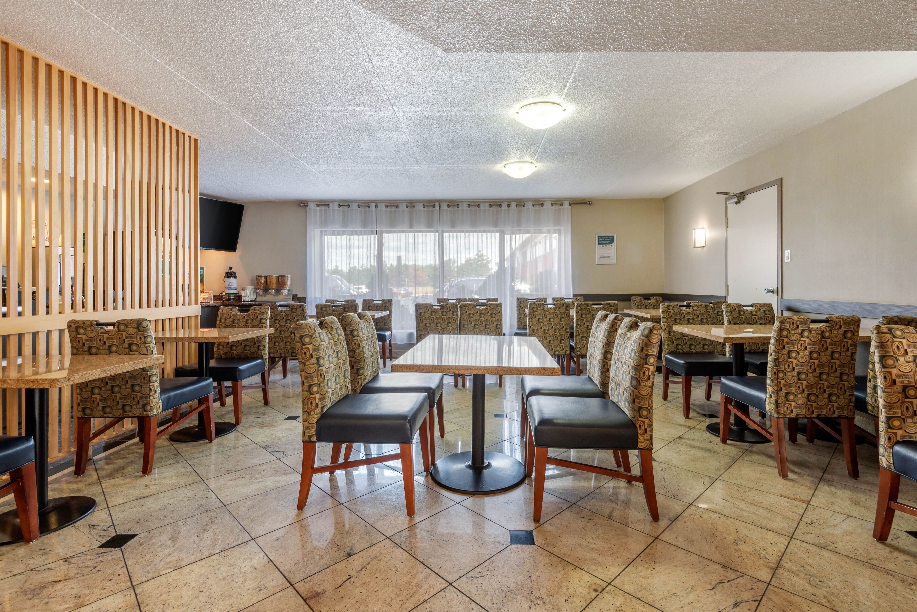 Un área de comedor con varias mesas y sillas, un separador de madera y un ventanal con cortinas.