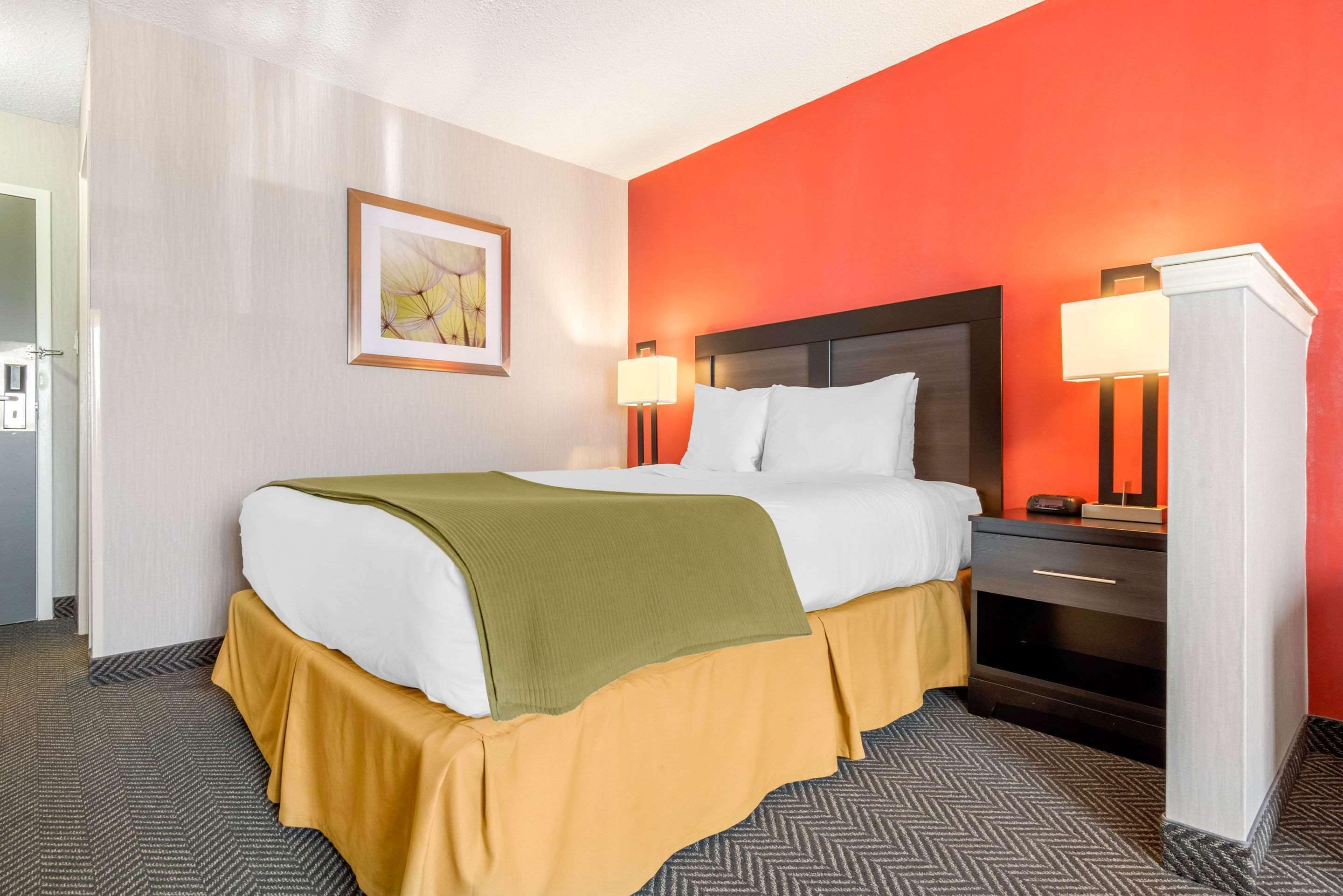 Quarto de hotel com uma cama, mesas de cabeceira, abajur e um quadro na parede.