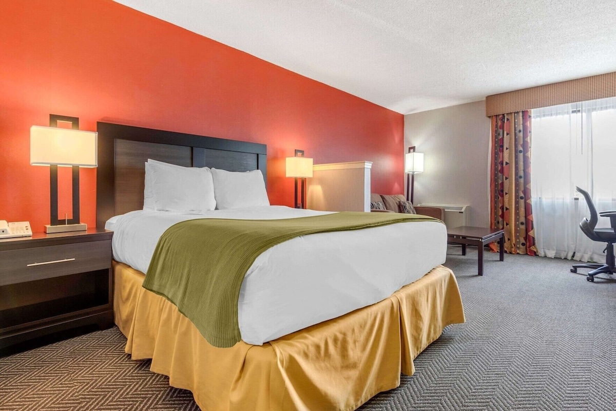 A hotel room with a large bed, bedside tables with lamps, a desk, and a chair.