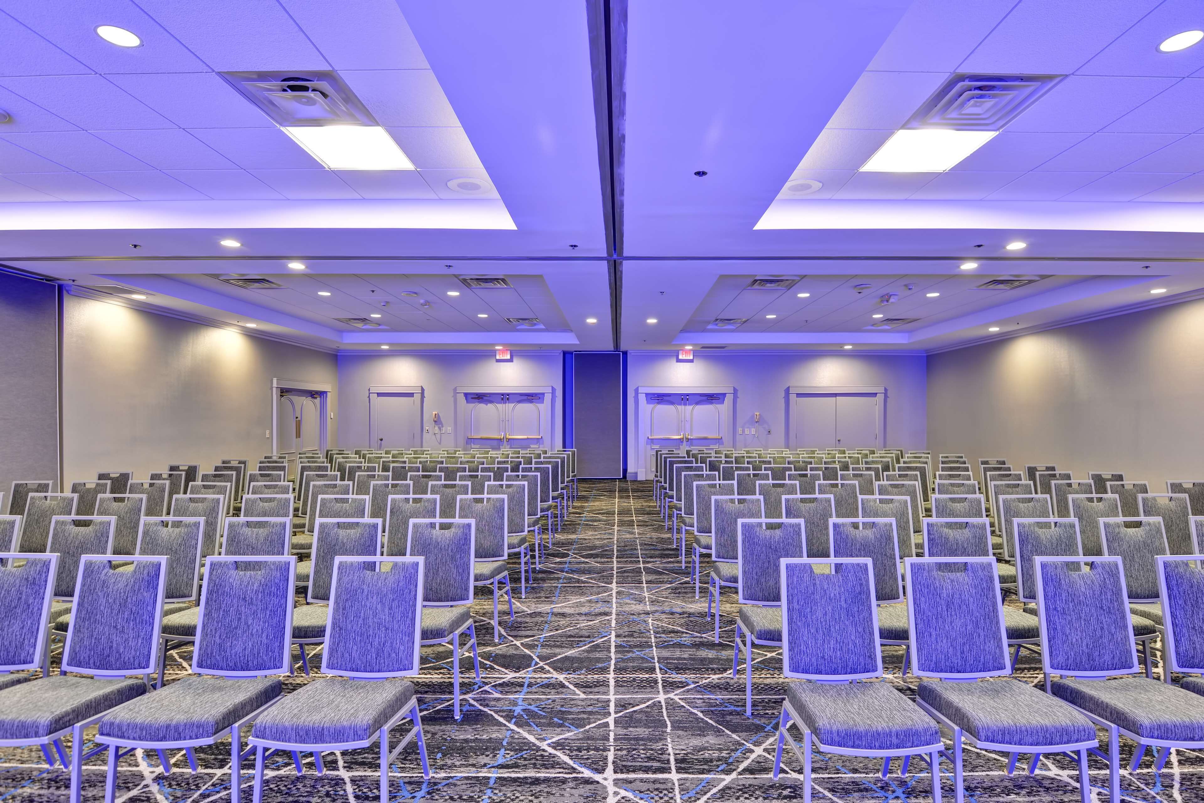 A conference room with rows of chairs, a carpeted floor, and a ceiling with recessed lighting.