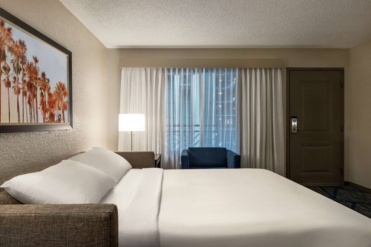 Een hotelkamer met een groot bed, een stoel, een bureau, een lamp en een deur.