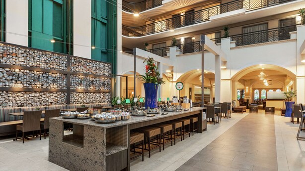 Spaziosa hall con una lunga reception, diverse aree salotto e un pannello decorativo con motivo a mosaico.