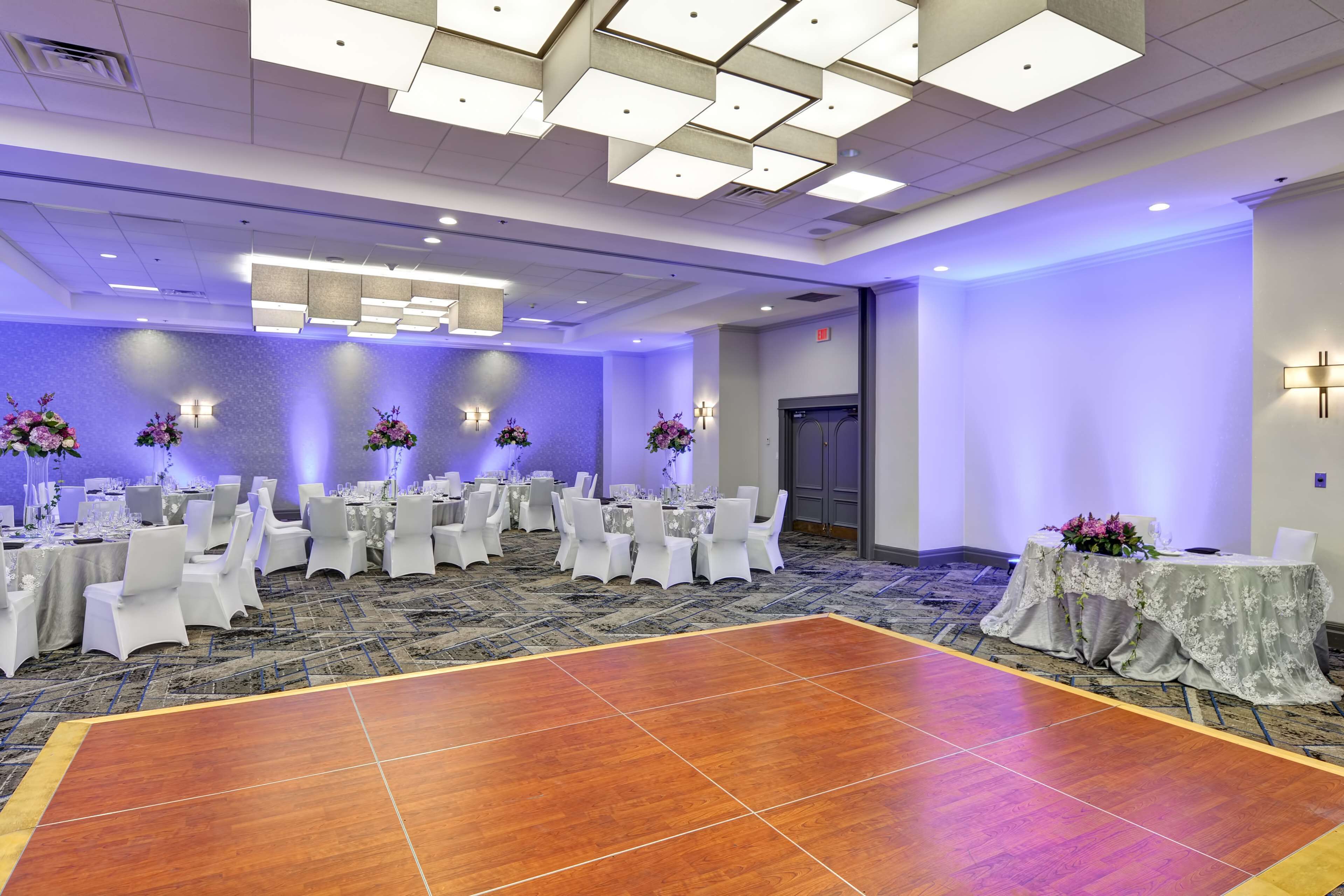 A conference room with tables set for a meeting, a dance floor, and a reception area with a counter and chairs.