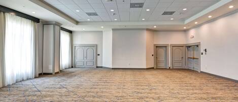 A large, empty conference room with a carpeted floor, white walls, and multiple doors.