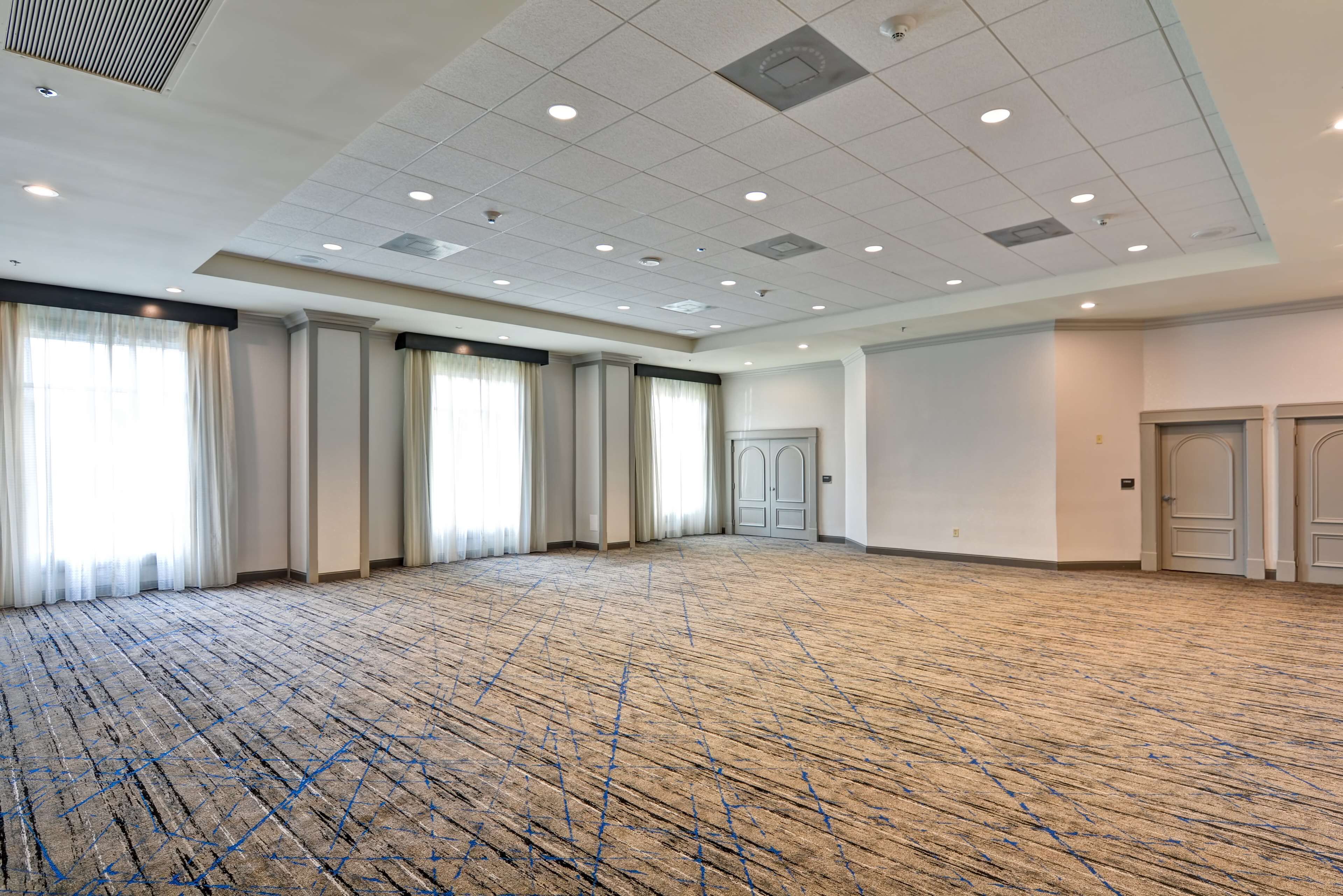 Une grande pièce vide, dotée d’un tapis à motifs, de murs blancs et d’un plafond haut avec des luminaires encastrés.
