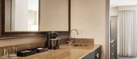 A hotel bathroom with a granite countertop, a sink, a mirror, and a cabinet with a lock.