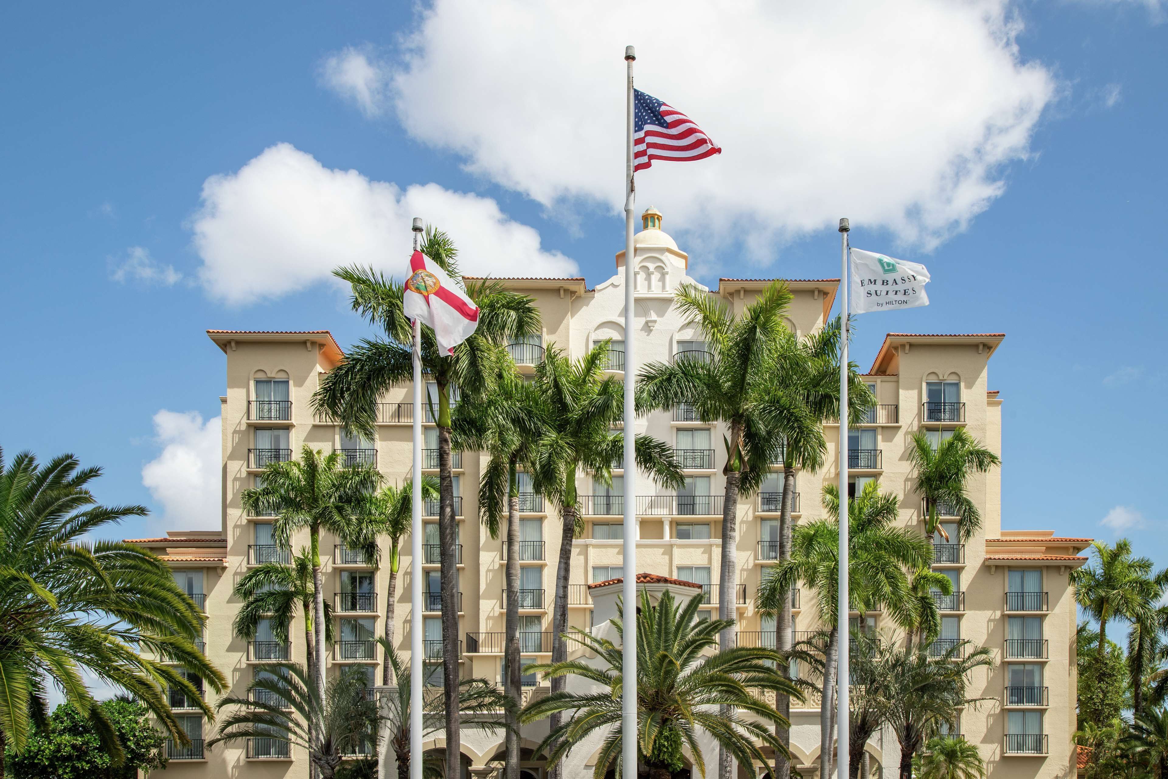 A multi-story hotel with a central tower, palm trees, and flags.
