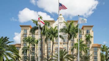 A multi-story hotel with a central tower, palm trees, and flags.