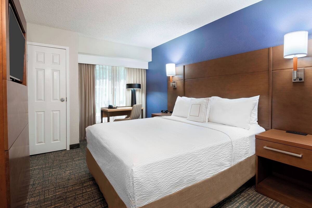 A hotel room with a large bed, a desk, a chair, a nightstand, and a TV.
