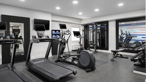 Une salle de sport moderne équipée de tapis de course, de vélos elliptiques et de matériel de musculation.
