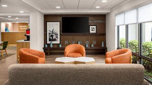 Un hall d’entrée avec un comptoir de réception, deux fauteuils orange, un grand téléviseur à écran plat et un mur orné de carreaux décoratifs et de tableaux encadrés.