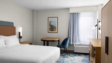 Habitación de hotel con cama, escritorio, silla, una mesita, un cuadro en la pared y ventana con cortinas.