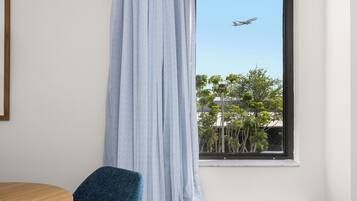 Ein Zimmer mit Fenster und Blick auf eine von Bäumen gesäumte Straße, ein Sessel und eine Heizung.