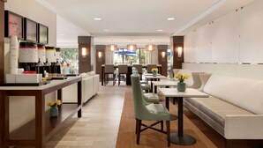 Un hall d’hôtel moderne avec un long comptoir d’accueil, un espace salon et des tables à manger.