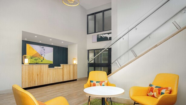 A modern lobby with a reception desk, two yellow chairs, a round table, and a staircase. - Spark by Hilton Brockville (Brockville)