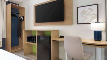Habitación de hotel pequeña con cama, escritorio con computadora, televisión de pantalla plana, microondas y refrigerador.