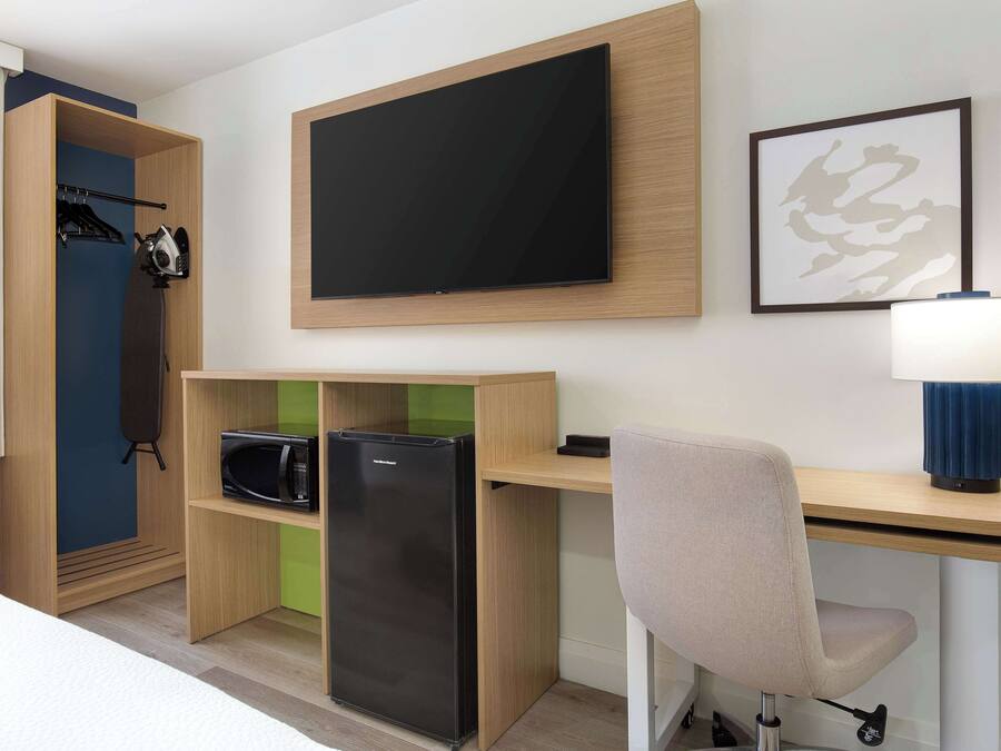 Habitación de hotel pequeña con cama, escritorio con computadora, televisión de pantalla plana, microondas y refrigerador.