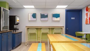 Una cocina moderna con armarios azules, un microondas y una cafetera. Hay tres cuadros enmarcados en la pared y una puerta azul con la etiqueta 'Solo Personal'.