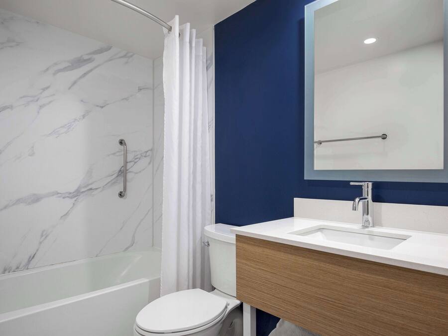 Une salle de bain moderne avec un mur de douche en marbre, des toilettes blanches, une baignoire entourée de parois en verre et un meuble-lavabo en bois avec un miroir.