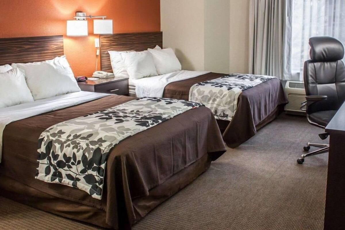 A hotel room with two beds, a desk, a chair, and a window with curtains.