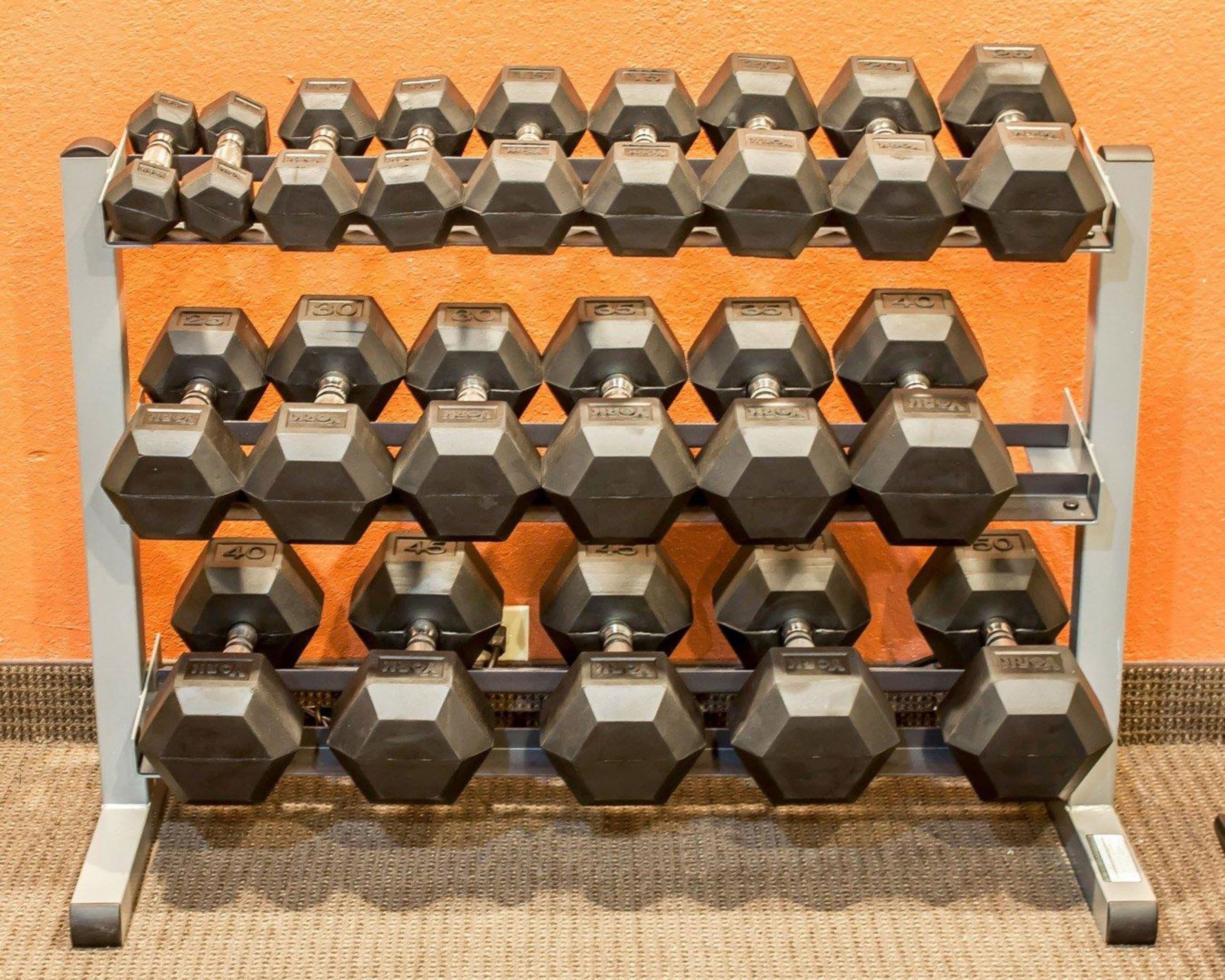 Un estante hexagonal con varias mancuernas de distintos pesos.