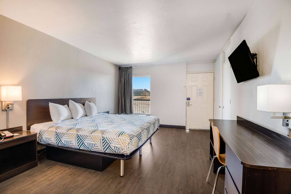 A hotel room with a bed, bedside table, desk, chair, and a TV mounted on the wall.
