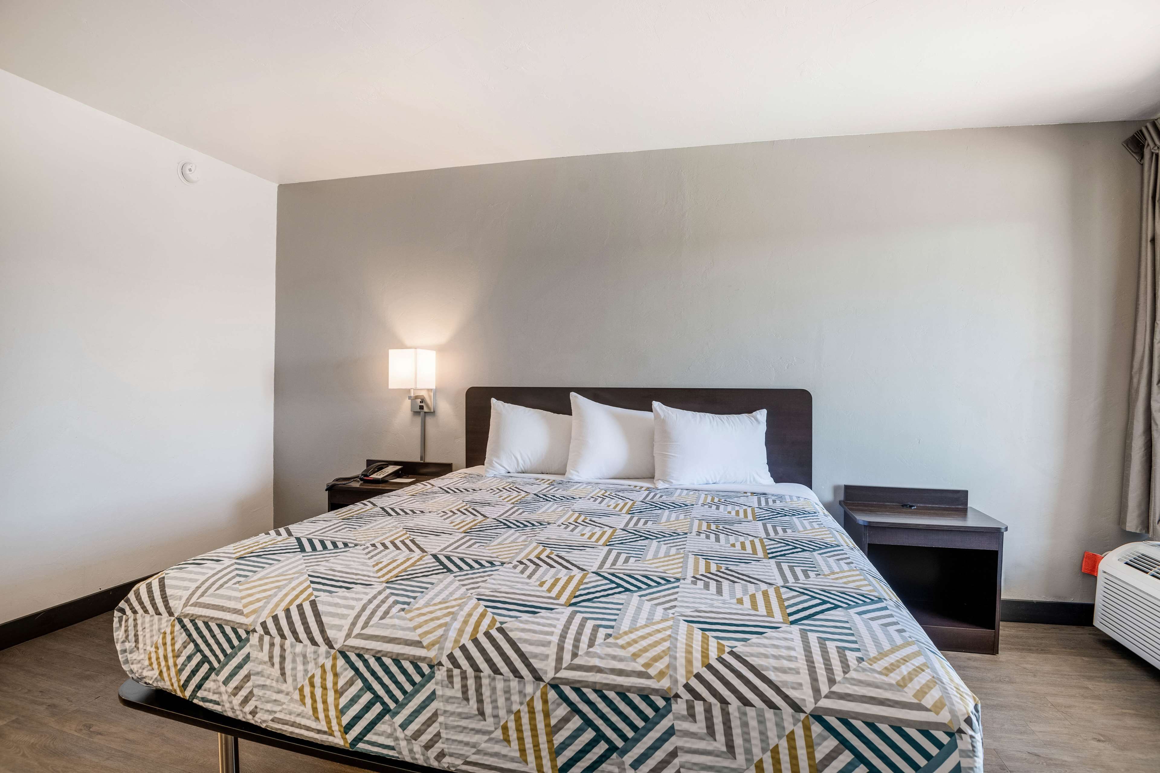Una habitació d'hotel amb un llit, una taula de nit, una làmpada i una finestra amb cortines.