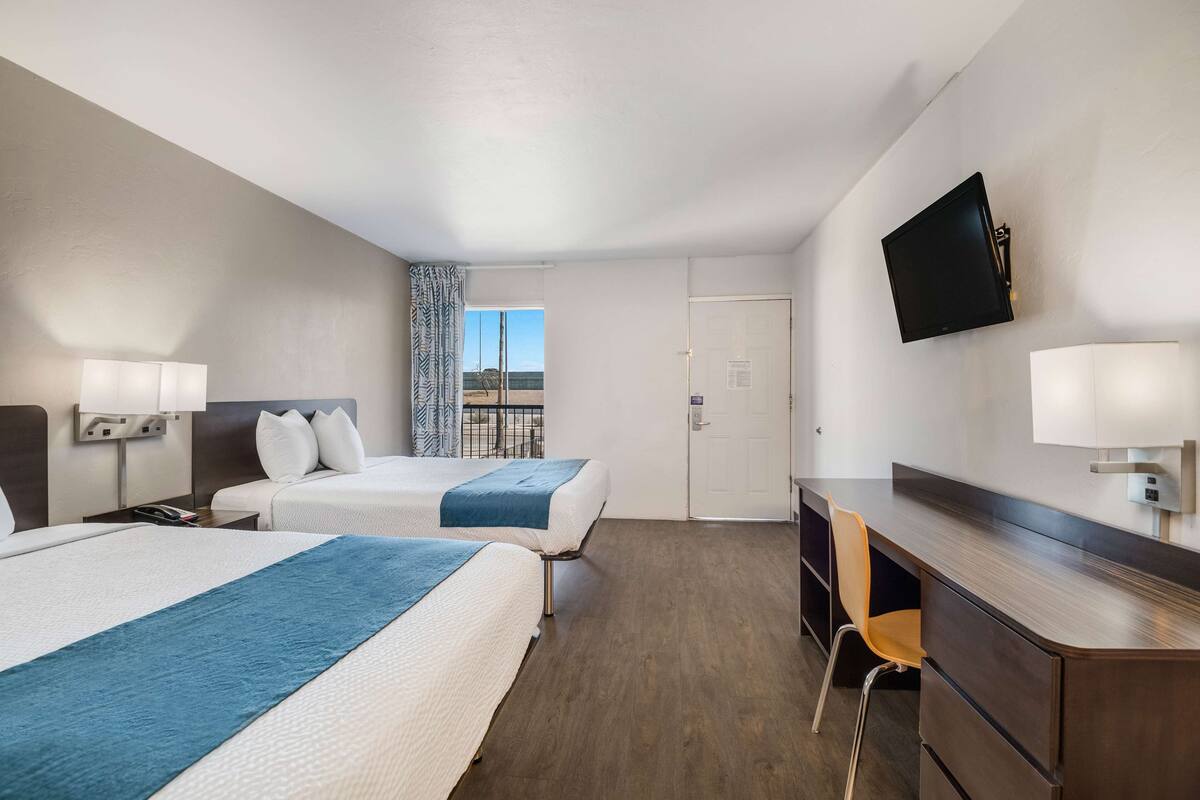 A hotel room with two beds, a desk, a chair, a TV, and a window with a view.