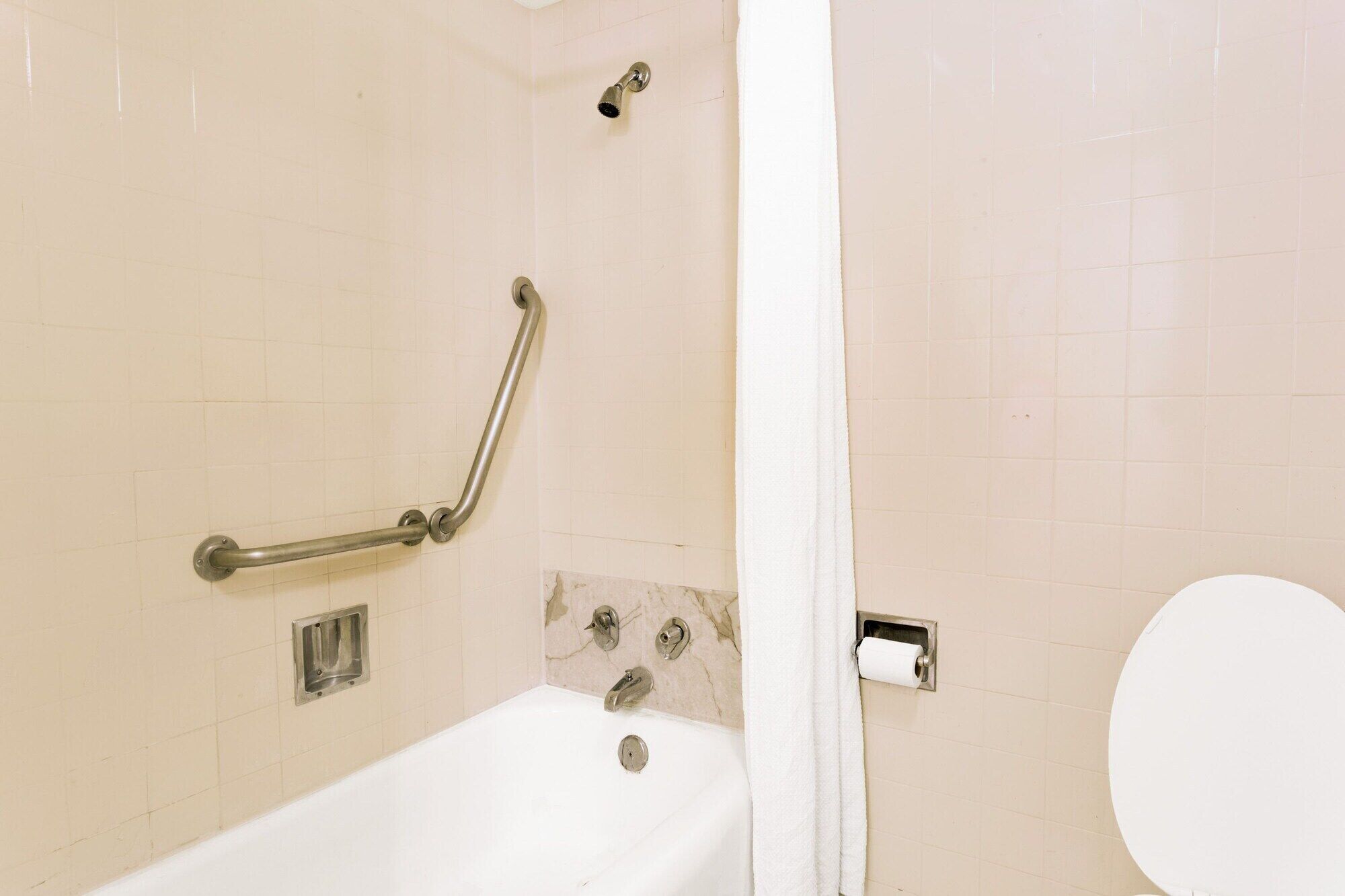 A bathroom with a bathtub, a handrail, a showerhead, a toilet, and a towel rack.