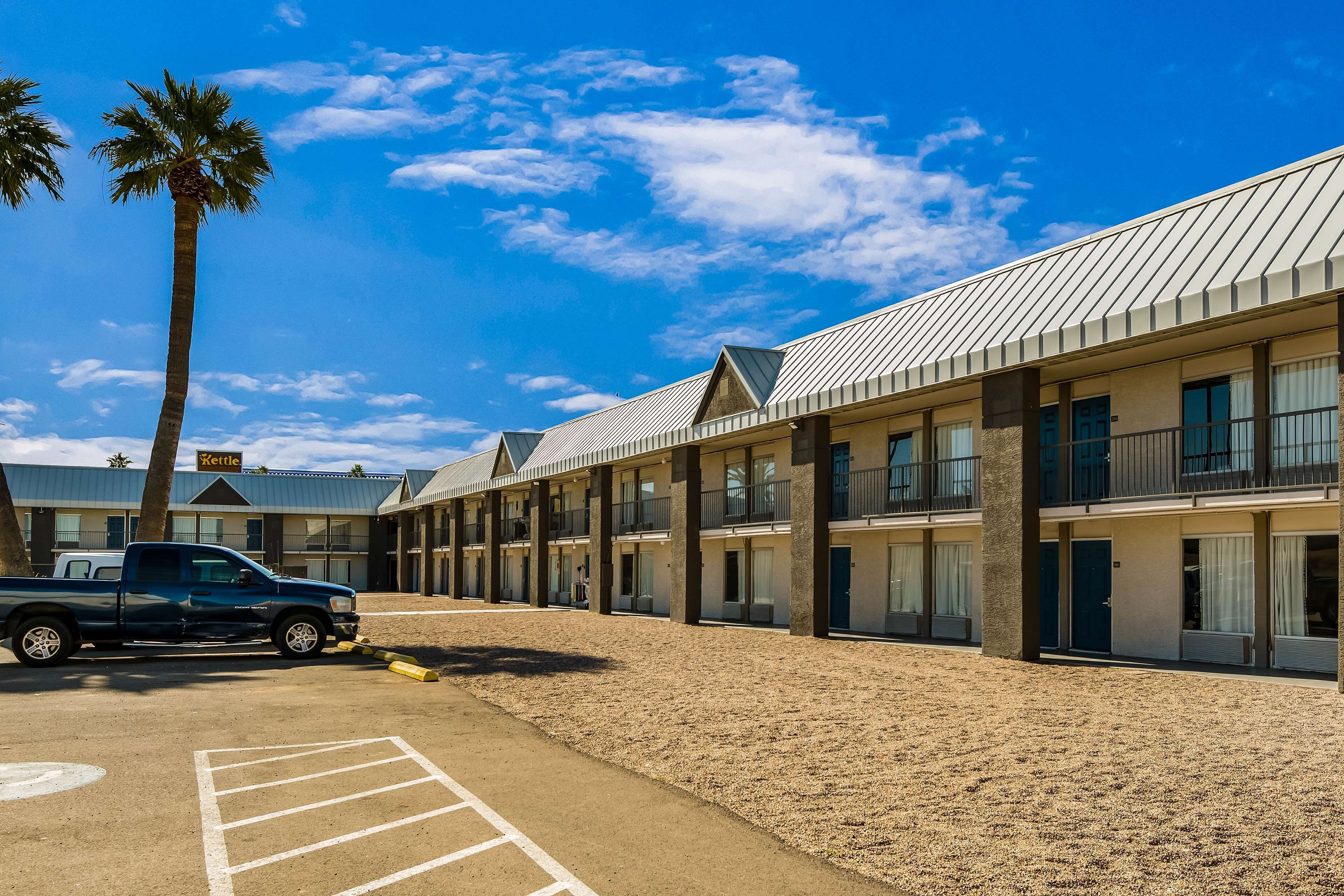 A motel with a parking lot, a blue pickup truck, and a palm tree.