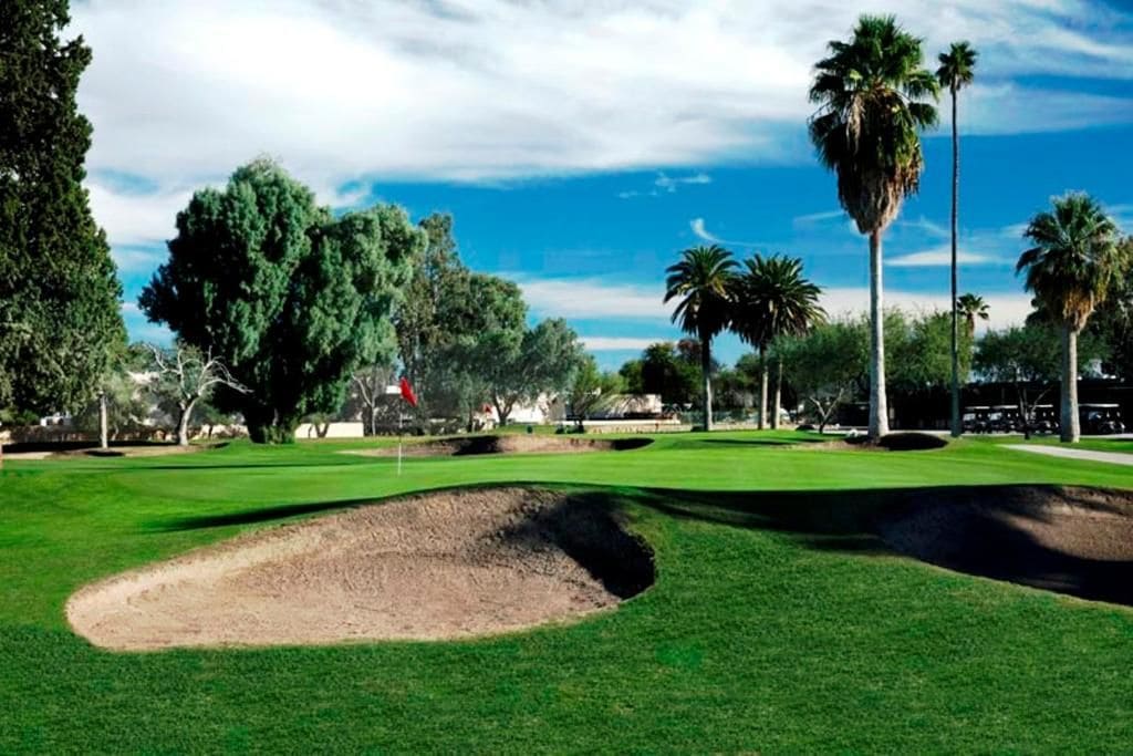 Een golfbaan met zandbunkers, palmbomen en een heldere lucht.