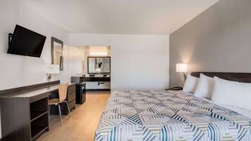 Habitación de hotel con cama, escritorio, silla, televisión, espejo y baño a la vista.