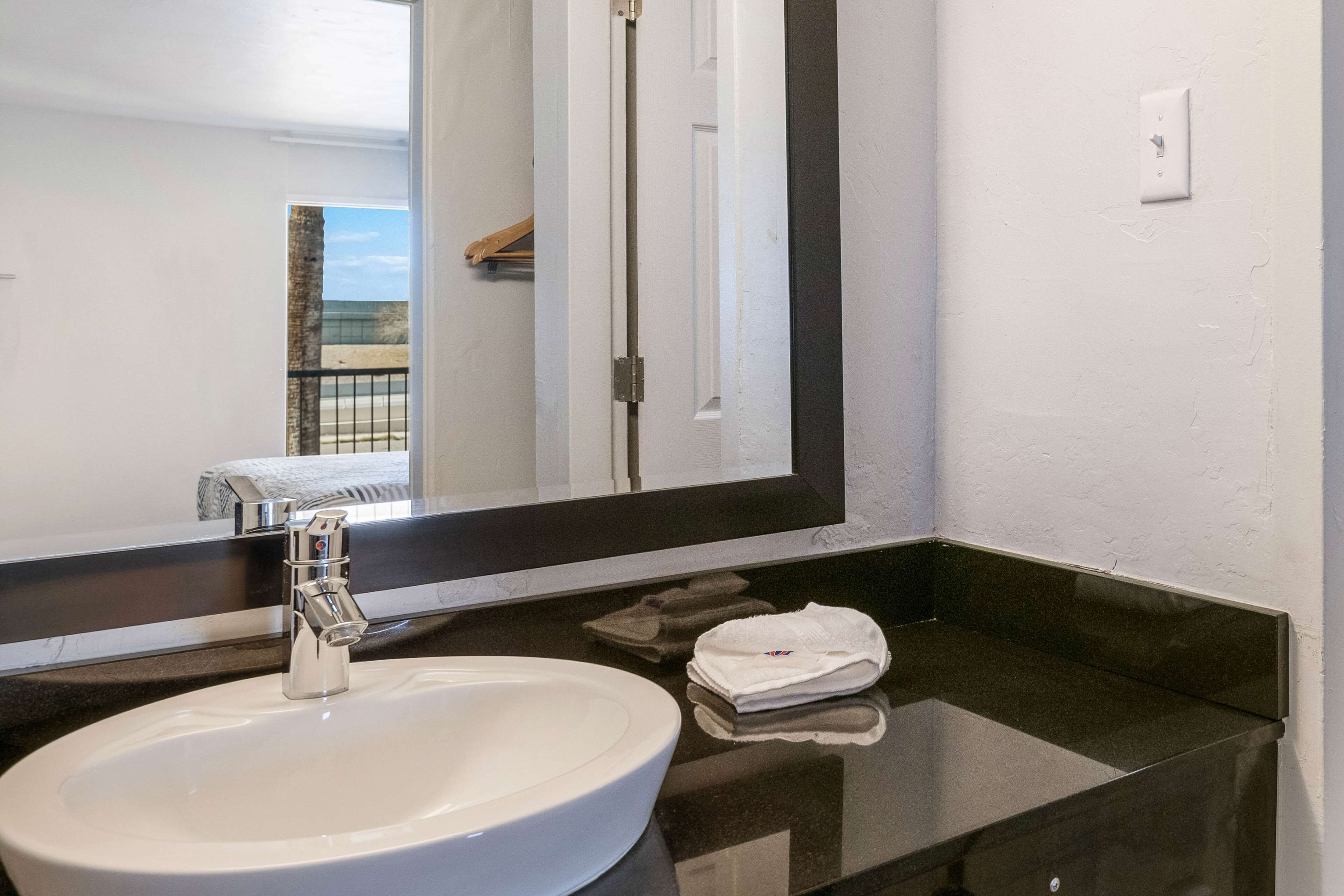 Un baño con un lavamanos blanco, un espejo grande y una encimera negra.