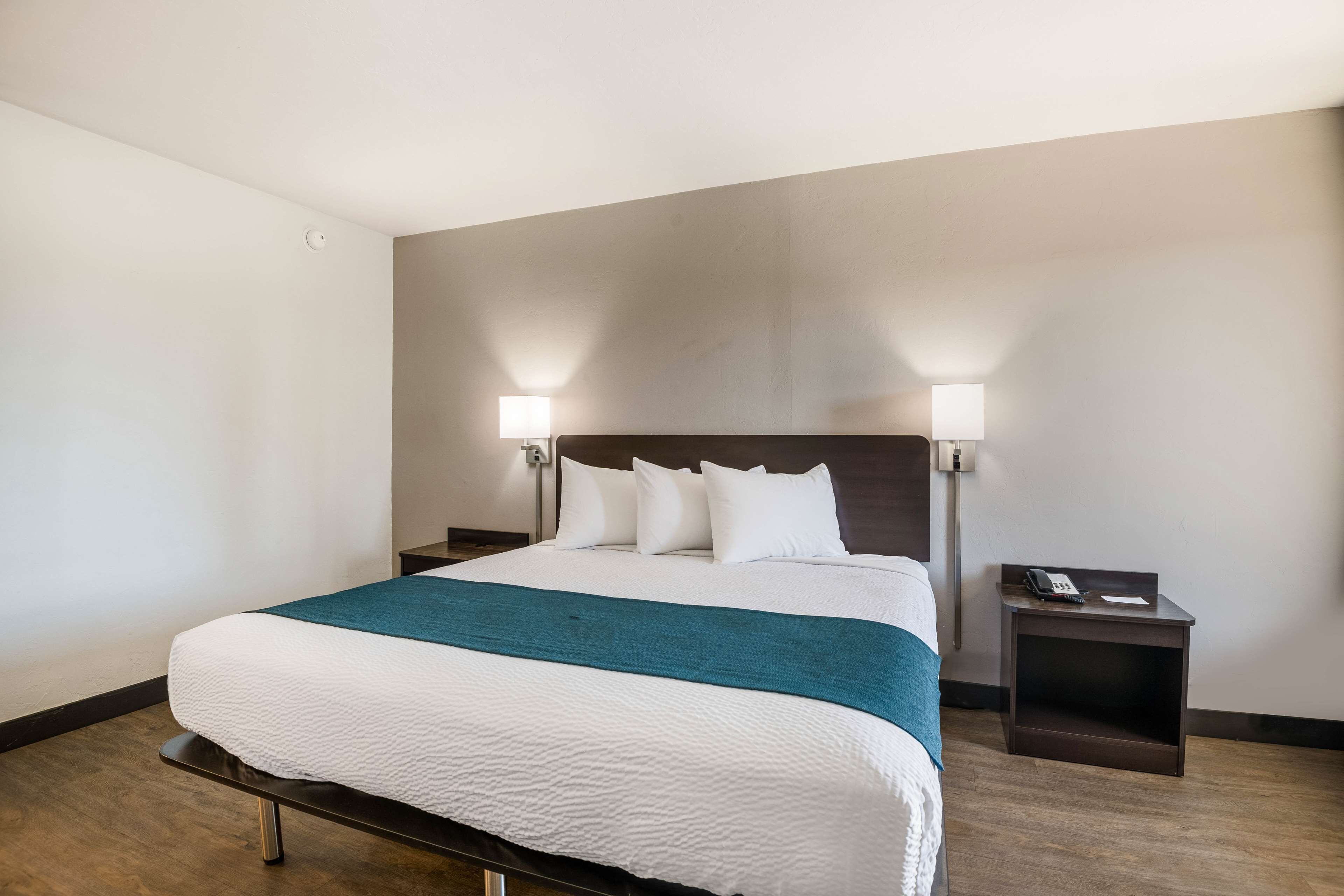 Une chambre d’hôtel avec un grand lit, deux lampes de chevet, une table de chevet avec un téléphone et un plaid de couleur turquoise.