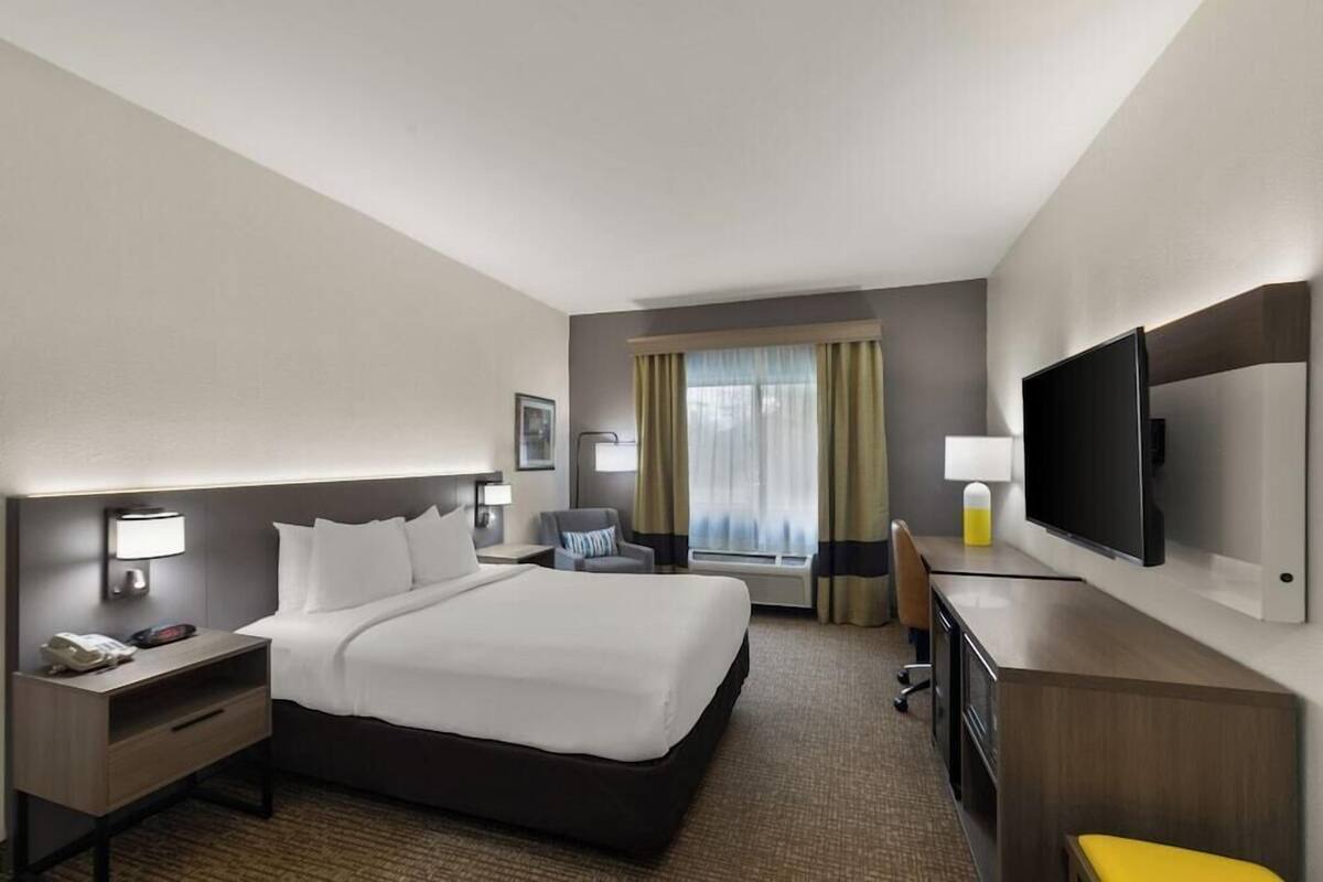 A hotel room with a large bed, a desk, a chair, a TV, and a window with curtains.