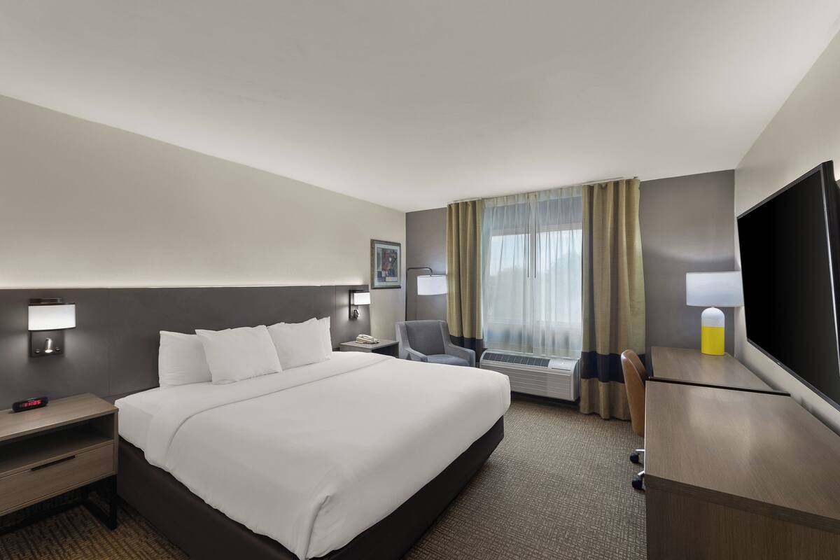 A hotel room with a large bed, a desk, a chair, a flat-screen TV, and a window with curtains.