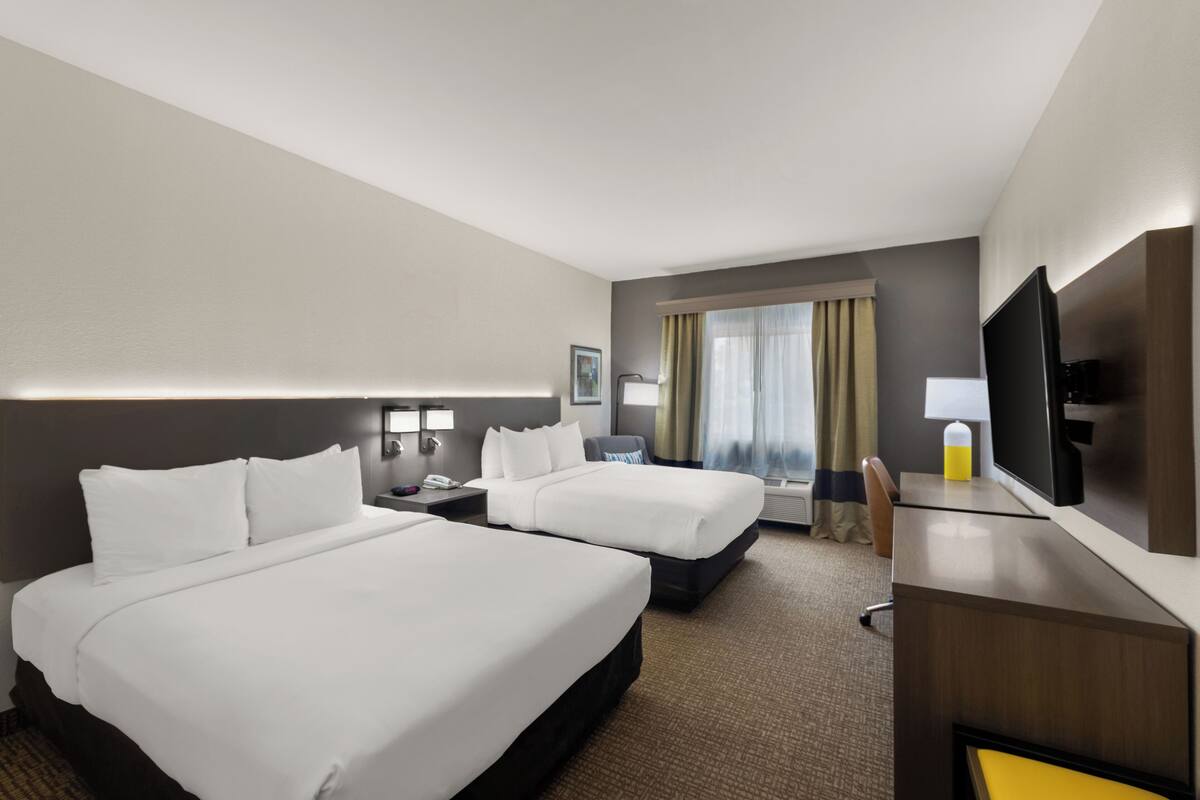 A hotel room with two beds, a desk, a TV, and a window with curtains.