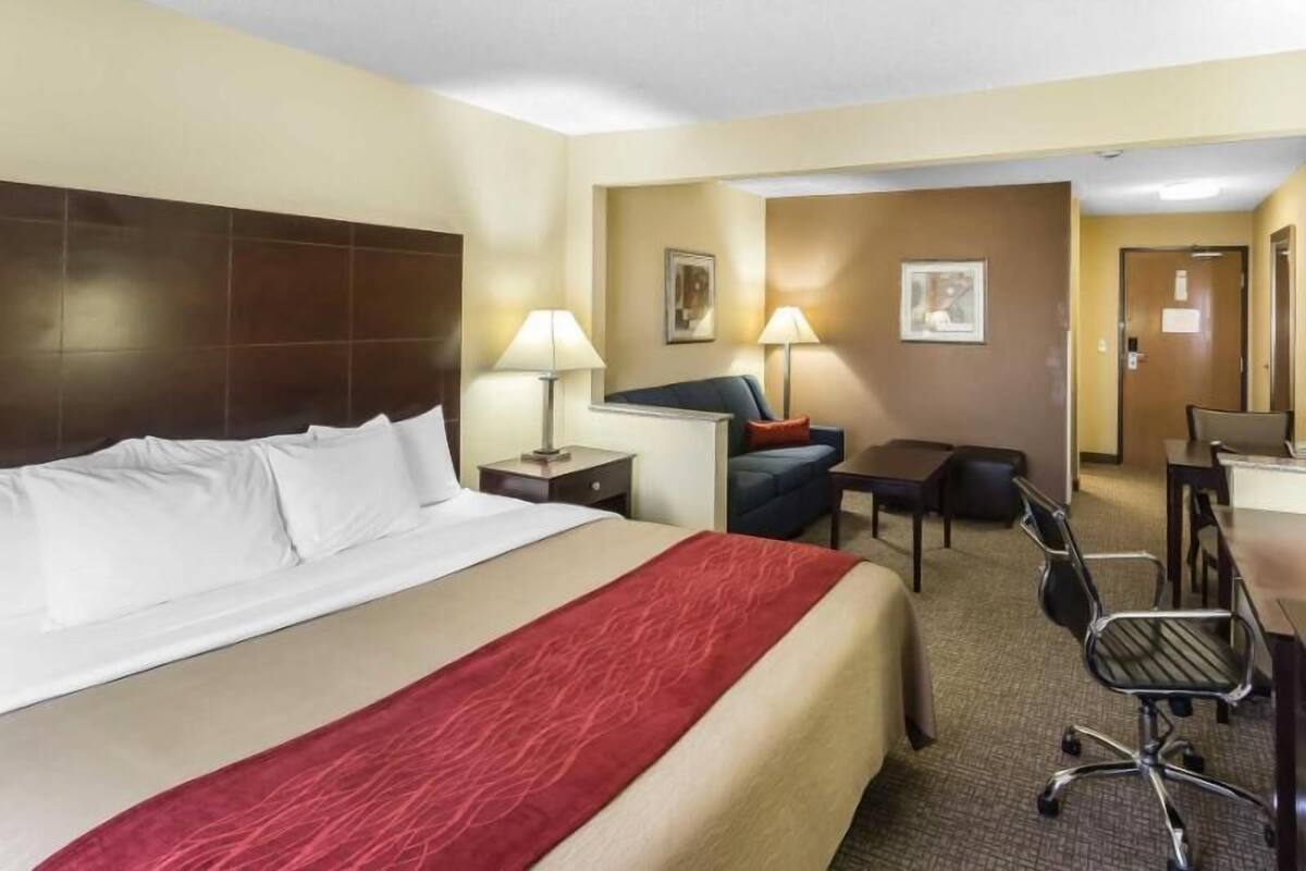 A hotel room with a large bed, a desk, a chair, and a lamp.