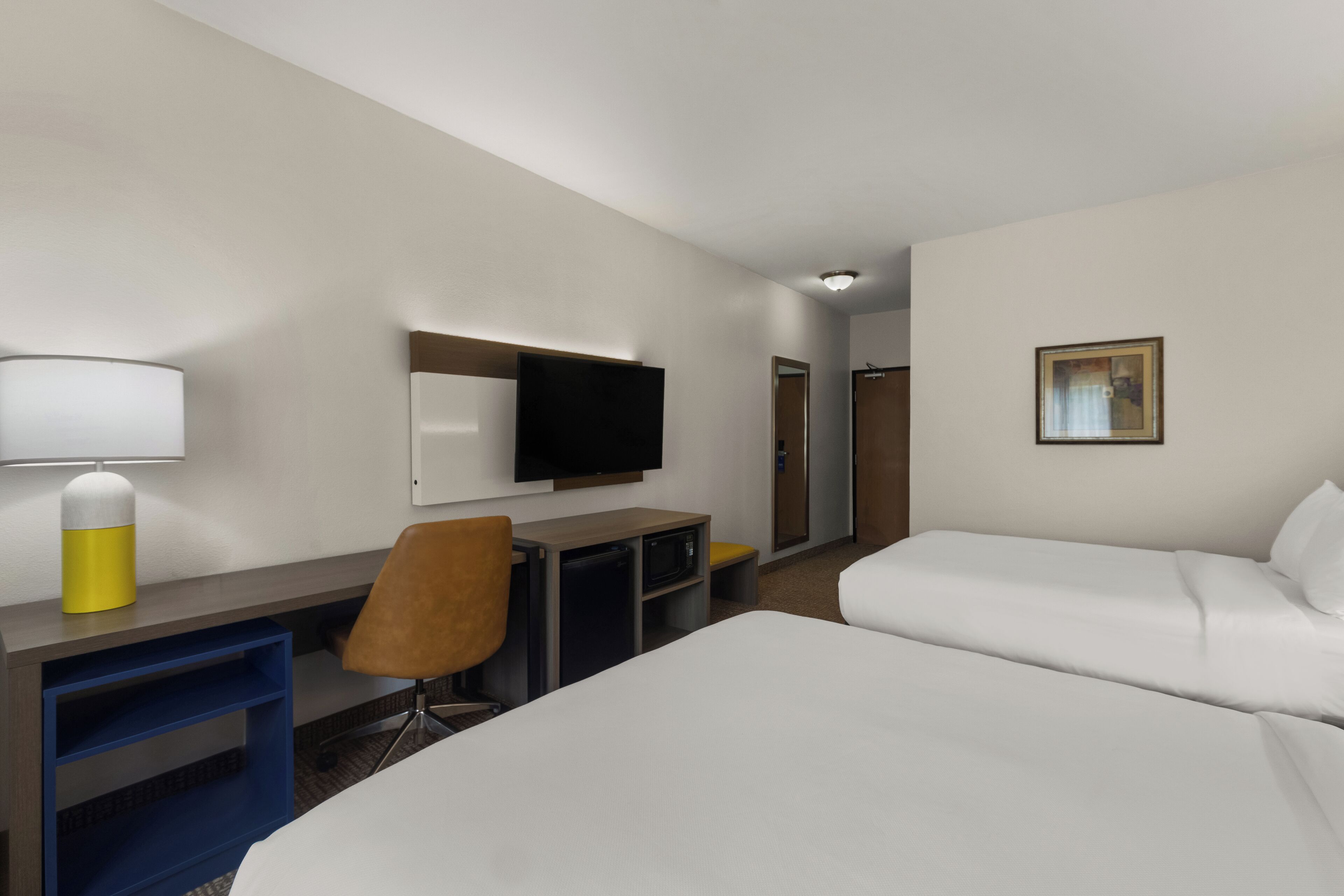 A hotel room with a bed, a desk with a chair, a television, and a painting on the wall.