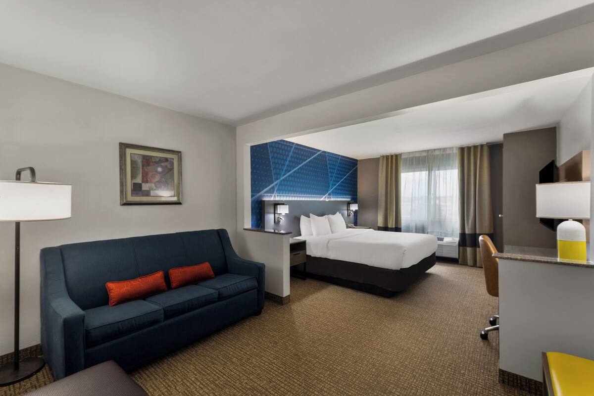 A hotel room with a bed, a sofa, a desk, and a large window with curtains.
