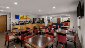 A hotel dining area with multiple tables and chairs, a kitchen area, and a television mounted on the wall. - Comfort Inn & Suites Austin North Loop (Austin)