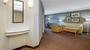 Una habitación de hotel con alfombra marrón, un sofá, una mesa de centro, un escritorio con silla y luces fijadas a la pared.