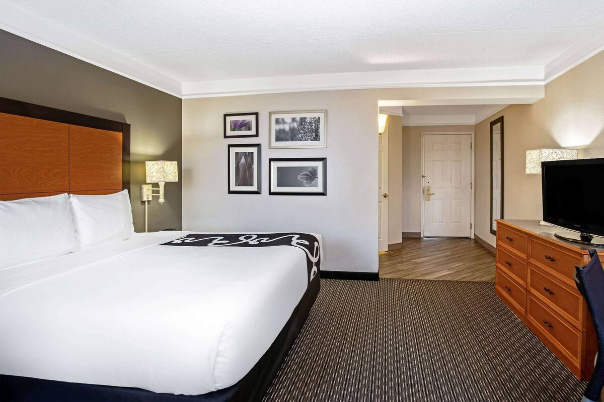 A hotel room with a large bed, a television, a dresser, and a door leading to another room.
