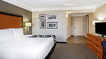 A hotel room with a large bed, a television, a dresser, and a door leading to another room.