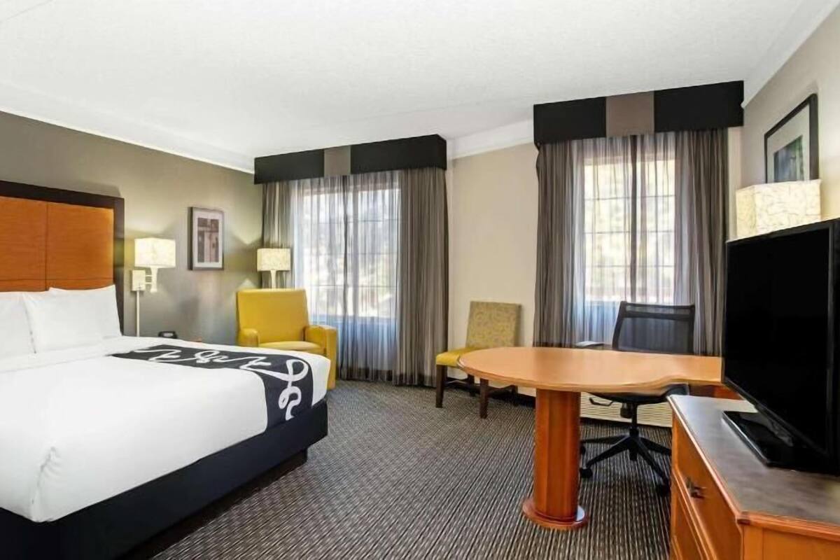 A hotel room with a large bed, a desk with a chair, a television, and two windows with curtains.